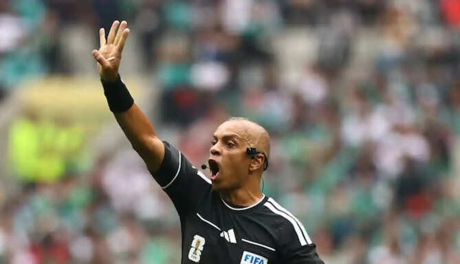 A FIFA World Cup 2026 referee using the new AI-powered Ref Cam technology during a football match.
