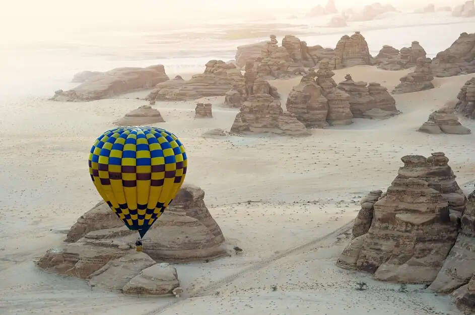 Hot air balloons flying over Hegra during AlUla Skies Festival with dramatic desert landscape and clear dark sky in Saudi Arabia.